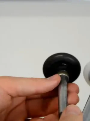 Close-up of a hand holding two garage door rollers for comparison, one with a black wheel and one with a white wheel, each attached to a metal stem.